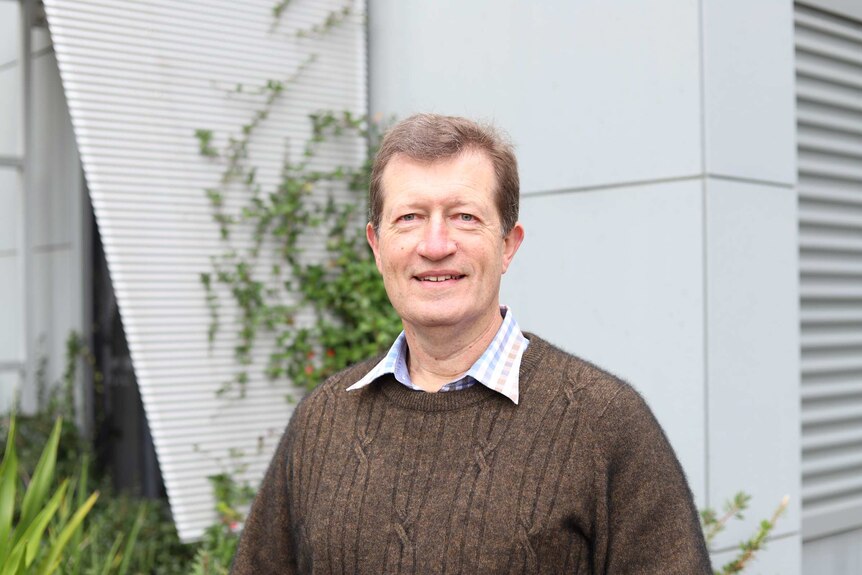 Man in jumper in front of wall.