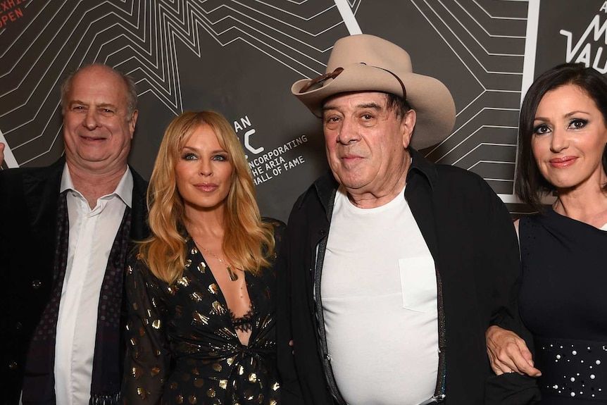 Michael Gudinski points his index finger in the air in a photo with Kylie Minogue, Molly Meldrum and Tina Arena.