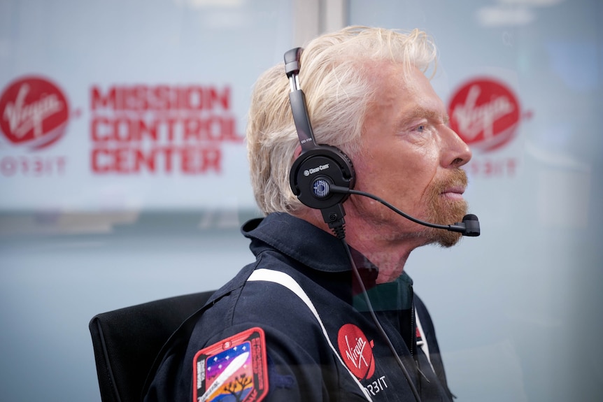 A bearded man with sandy hair – Richard Branson – wearing a headset and dark overalls.