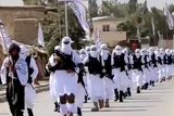 Dozens of Taliban fighters march in white uniforms down a street