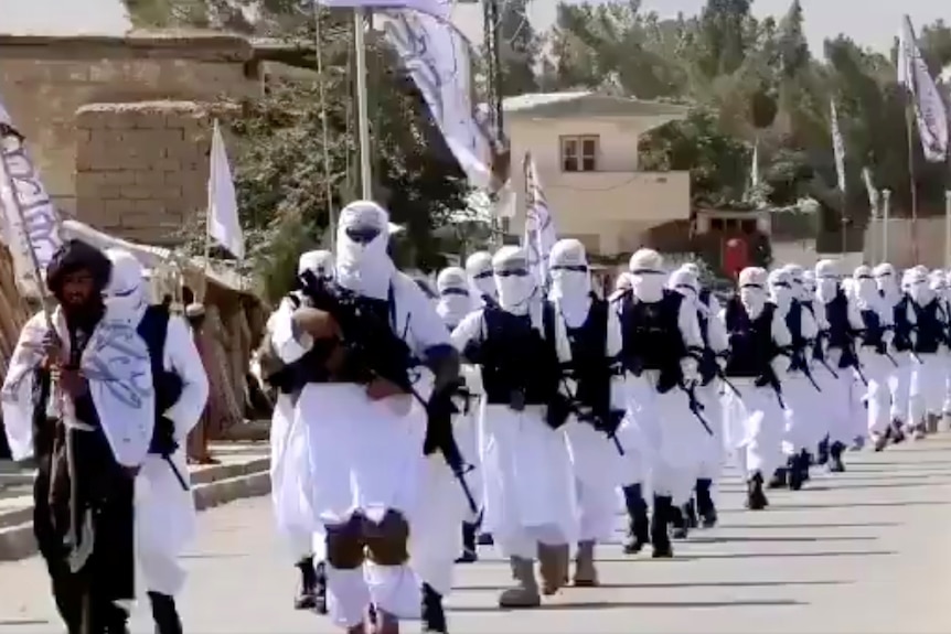 Dozens of Taliban fighters march in white uniforms down a street