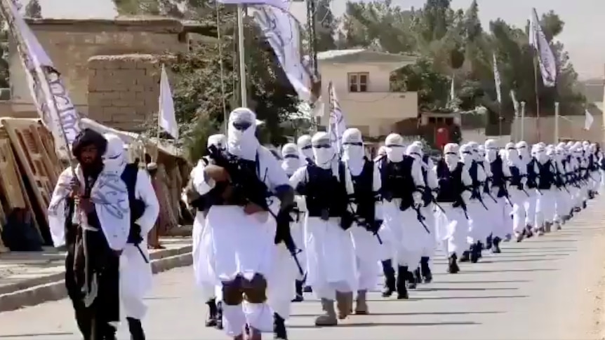 Dozens of Taliban fighters march in white uniforms down a street