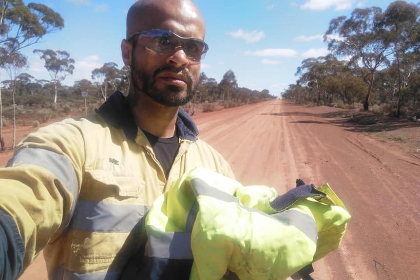 A man wearing high-vis workwear takes a selfie on a dusty outback road