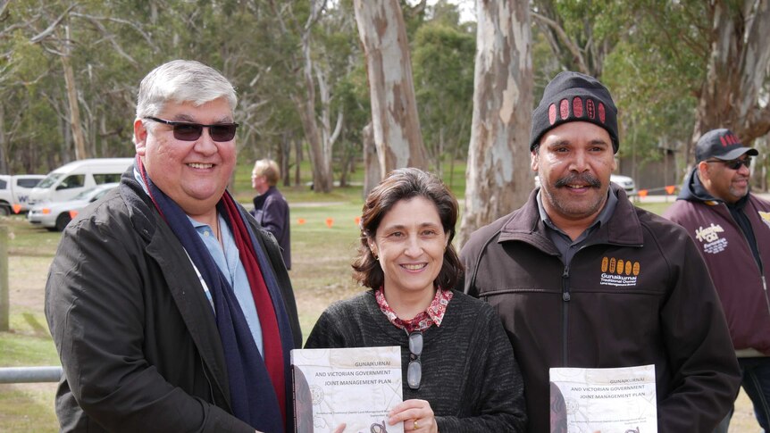 Two men and a woman pose together holding copies of the Gunaikurna and Victorian government joint management plan.