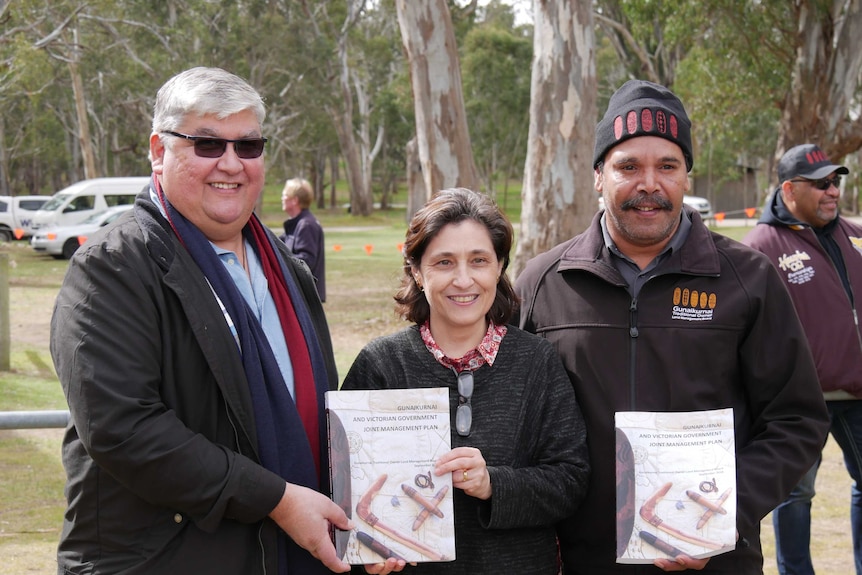Two men and a woman pose together holding copies of the Gunaikurna and Victorian government joint management plan.