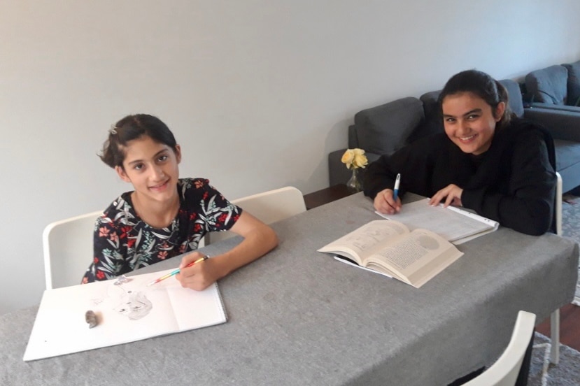 Two girls sitting at a desk with books in front of them. 