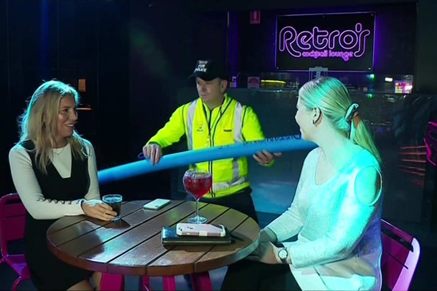 A man in high-vis uses a pool noodle to separate two women at a nightclub.