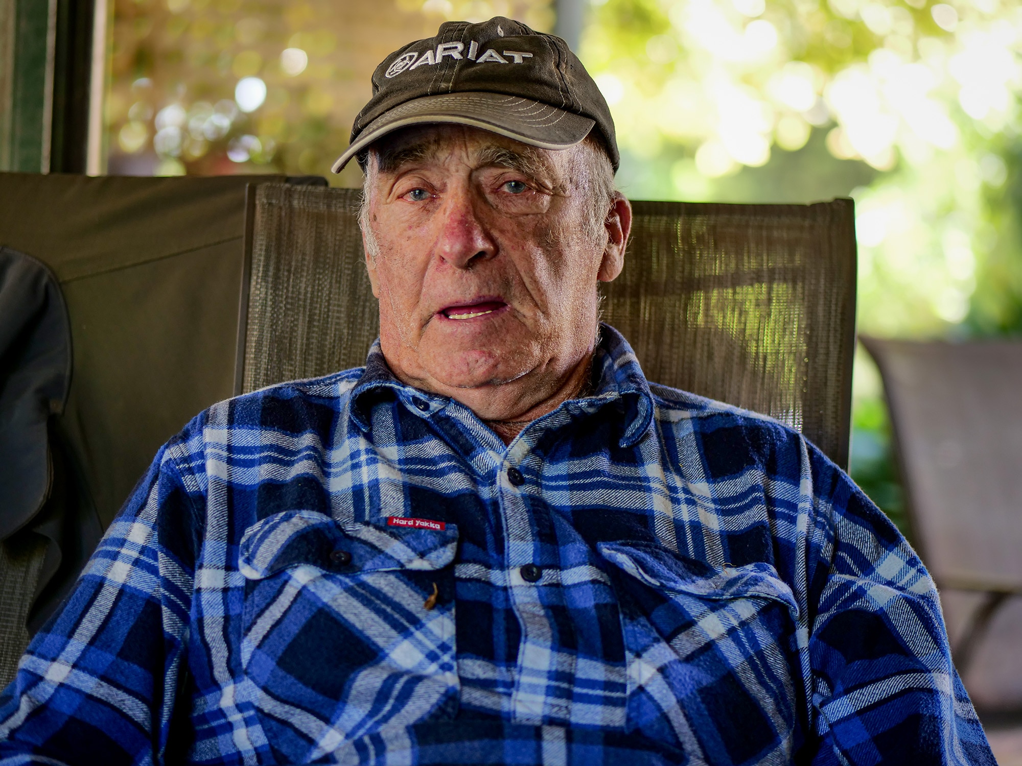 Ron Woodall sits in a chair wearing a blue shirt and black ariat cap