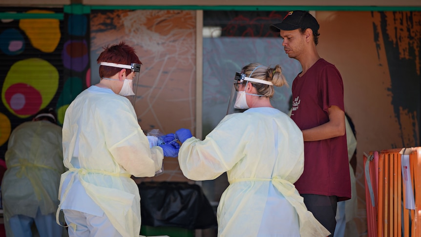 A man speaking to two people dressed in PPE outside a COVID-19 testing site.