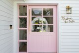 A pastel pink front door to a white multi-storey weatherboard house. 'Maison de rose' sign on the right