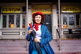 Young woman dressed as Mary Poppins outside old building.