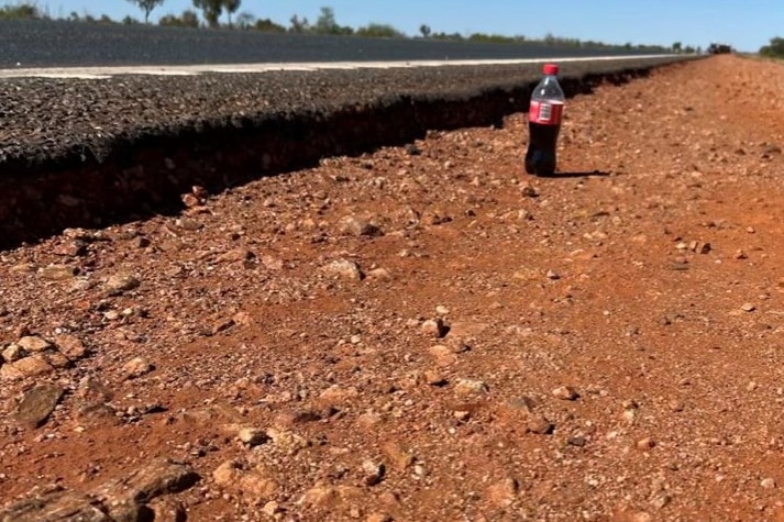 A small bottle of coke showing the depth of the drop-off on the side of a road.