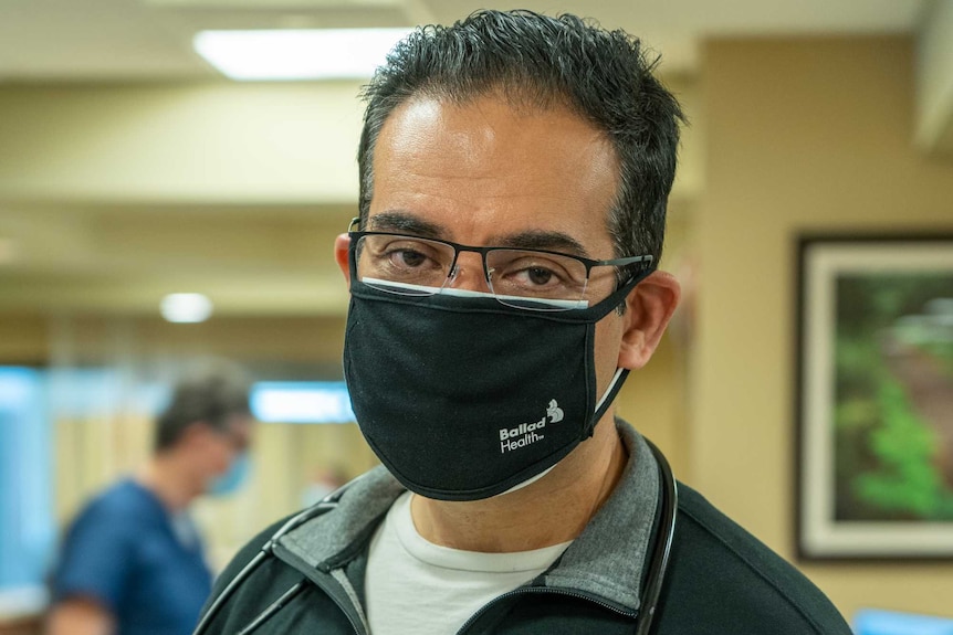 A man in a black face mask standing in a hospital ward