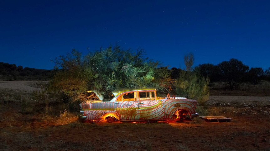 A car painted with orange and gold lines and dots, illuminated against a night sky