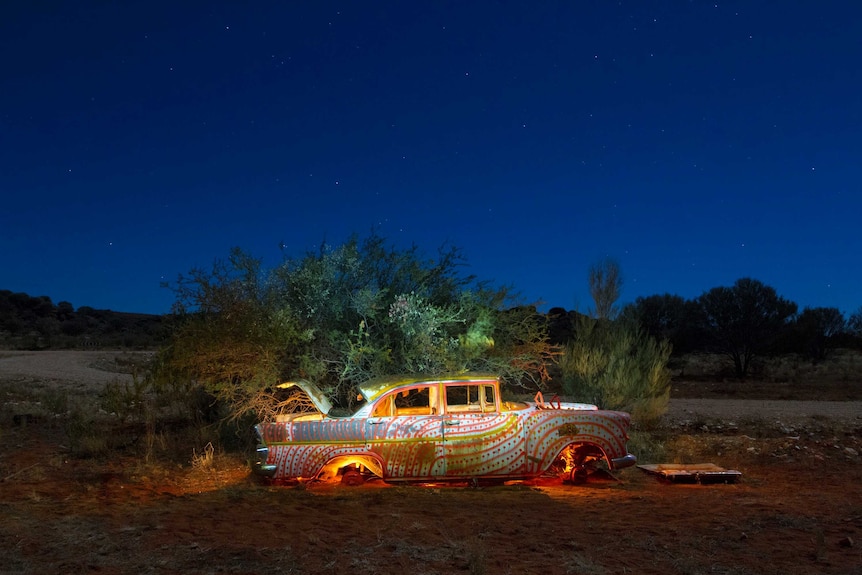 A car painted with orange and gold lines and dots, illuminated against a night sky