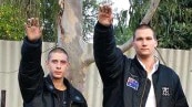 Two men in black jackets give a white power salute in a suburban backyard.