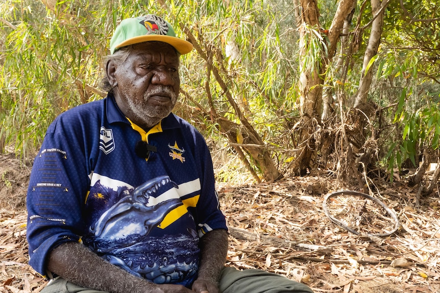 An older man sits in bushland on a creek bed