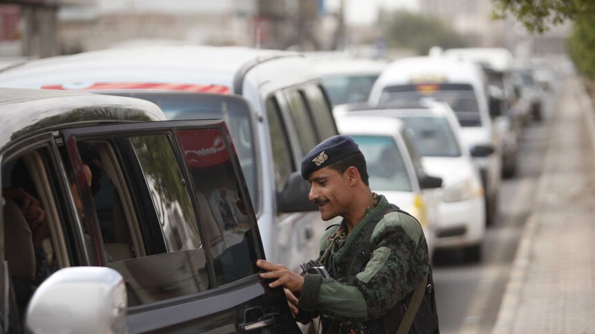 A police trooper checks a car at a checkpoint on the road leading to Sanaa International Airport.