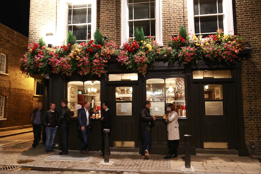 People standing and drinking in front of a British pub.