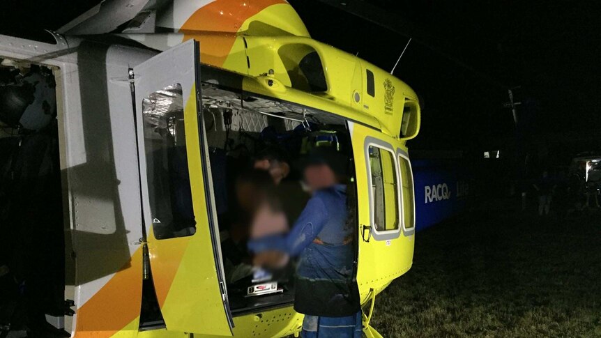 A yellow, orange and blue RACQ helicopter is seen with doors open as paramedic attends to blurred child.