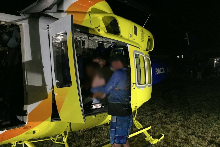 A yellow, orange and blue RACQ helicopter is seen with doors open as paramedic attends to blurred child.