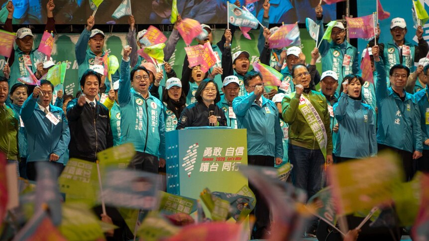 Tsai Ing-wen holds a microphone and speaks while supporters hold flags and cheer.