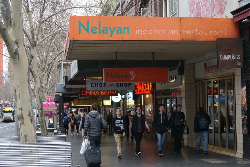 People walking along a busy street past Nelayan restaurants in Melbourne.
