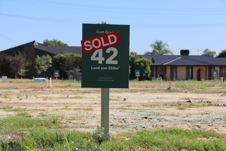 A 'sold' sign on an empty housing block with houses in the background.