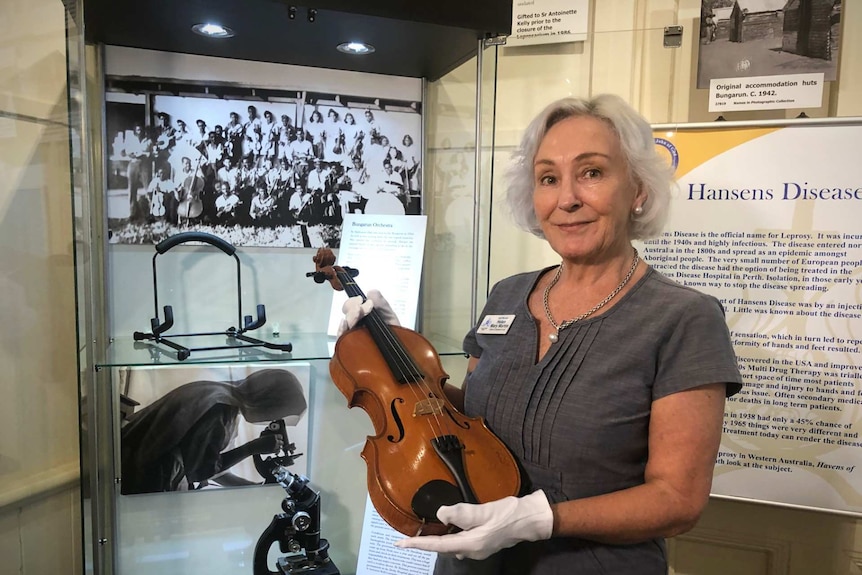 A woman wearing protective gloves holds a violin on display in a cabinet at a museum