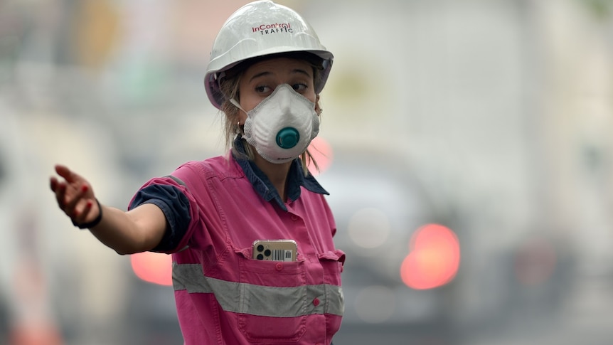 A woman wearing a respirator and a hard hat directing traffic