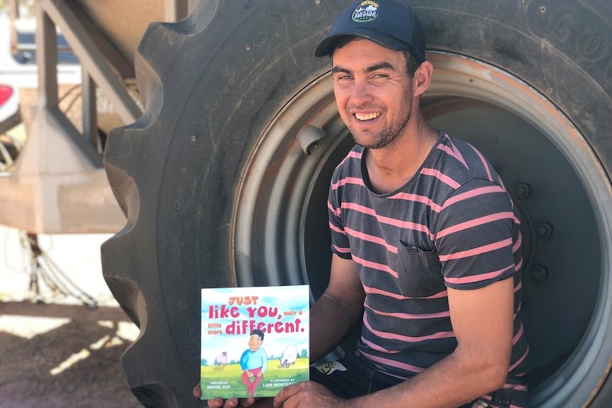 Man in striped shirt sitting in rim of large tractor tyre holding up children's book