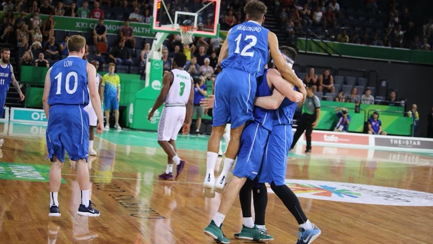 Scotland's basketball team celebrate by embracing during a game against Nigeria as the shot clock expires in the background.