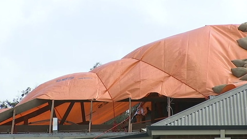 A house roof partly covered in an orange tarpaulin.