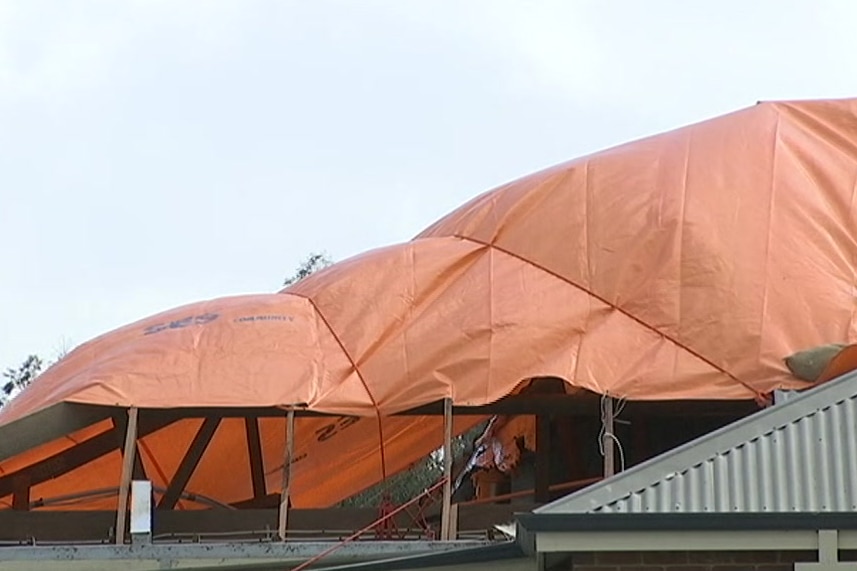 A house roof partly covered in an orange tarpaulin.