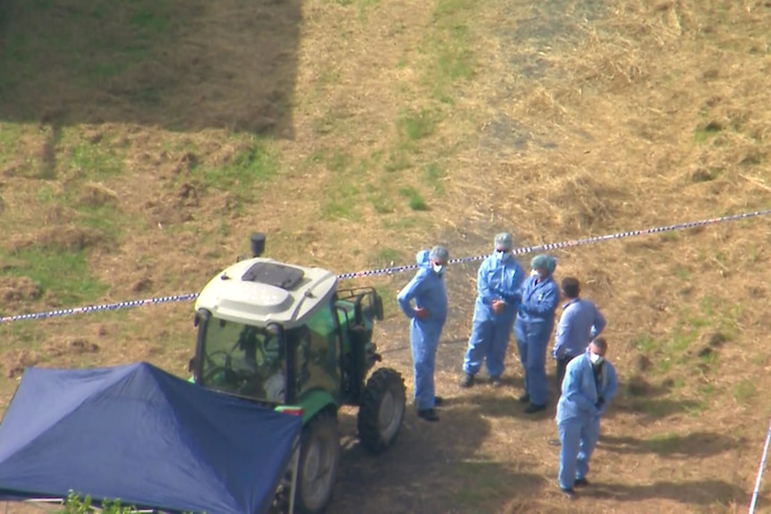 An aerial view of police forensic officers beside a tractor partially covered by a canopy