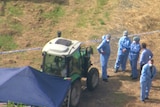 An aerial view of police forensic officers beside a tractor partially covered by a canopy