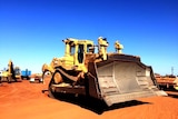 A close shot of a large bull dozer on red dirt. Blue sky and other machinery is in the background.