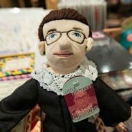 A Ruth Bader Ginsburg doll complete with lacy collar and glasses