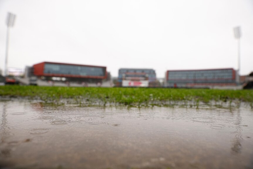 Large puddles on the grass with the Old Trafford stands visible in the background