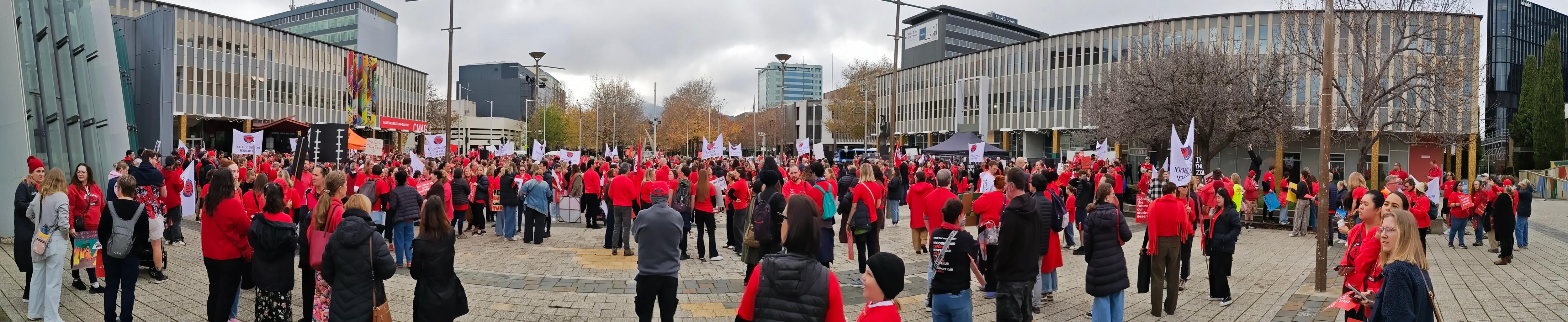 A group of people wearing red gathers outside a building, holding signs.