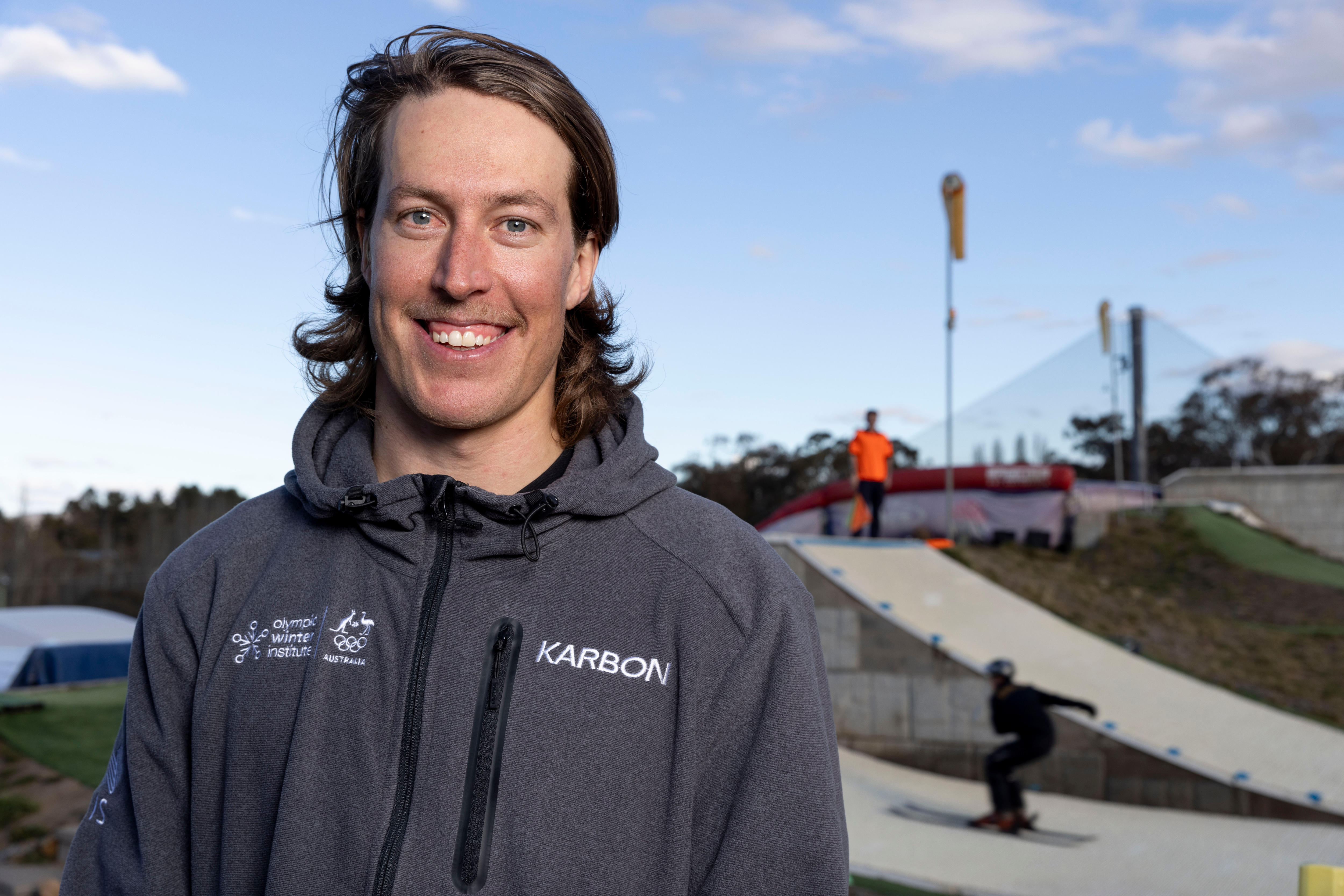 Un hombre con un suéter se encuentra frente a un salto de esquí. 
