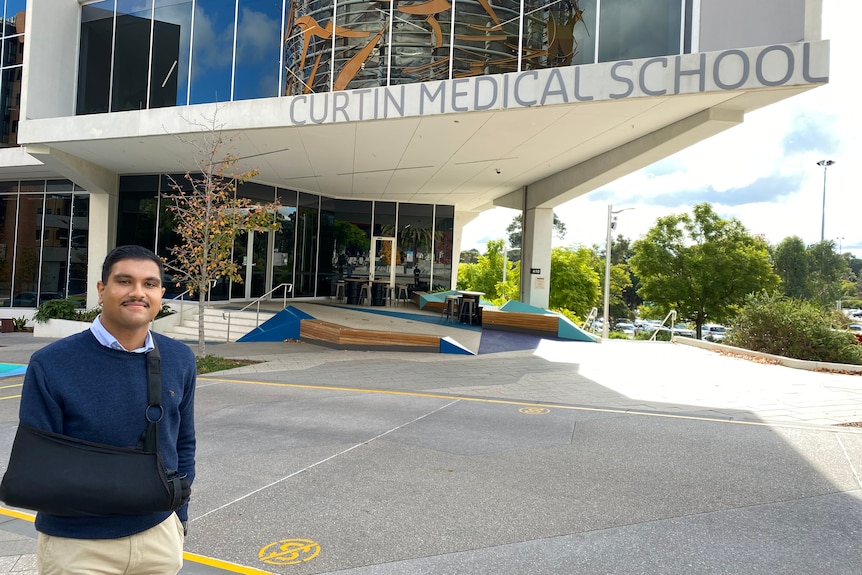 Michael Thomas standing outside Curtin Medical School wearing a sling