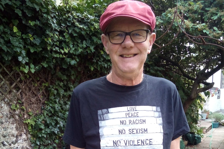 Mature-aged man wearing thick black framed glasses and a cap.