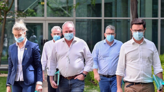 Four men and a woman wearing masks walk in a line carrying documents.