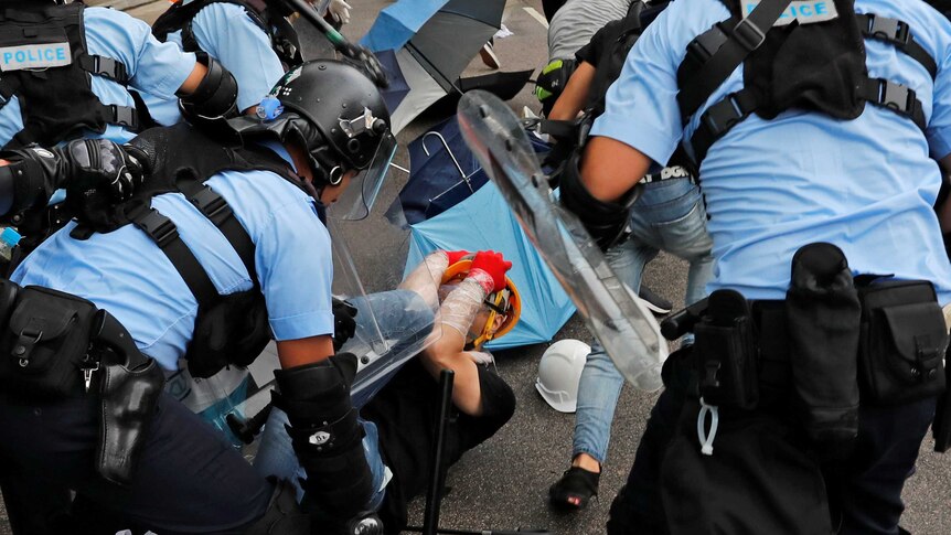 Riot police hit a protester lying on the ground and covering his face with his hands.