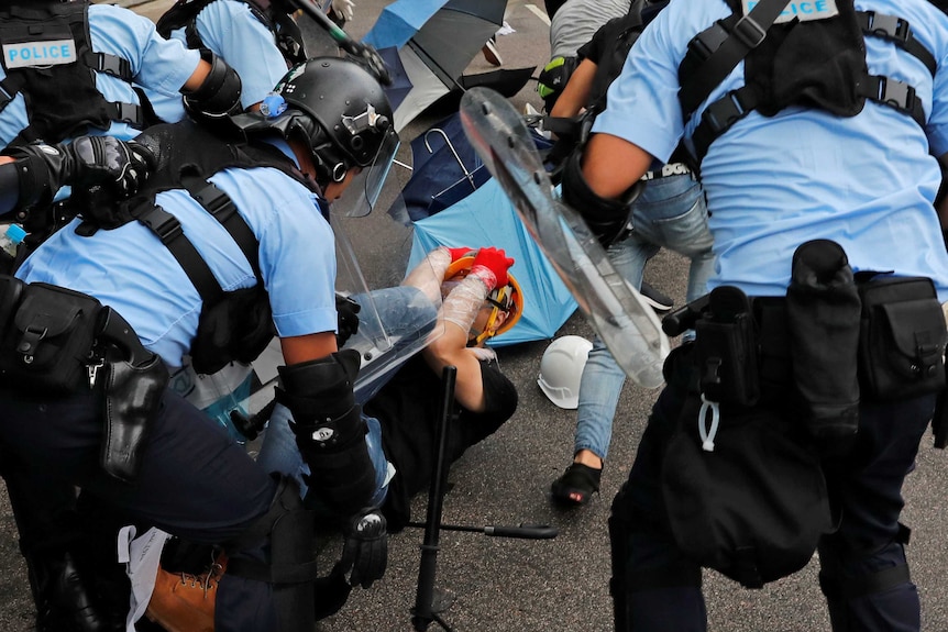 Riot police hit a protester lying on the ground and covering his face with his hands.