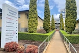 The outside of the Toowoomba Hospital, including a sign and walkway lined with trees.