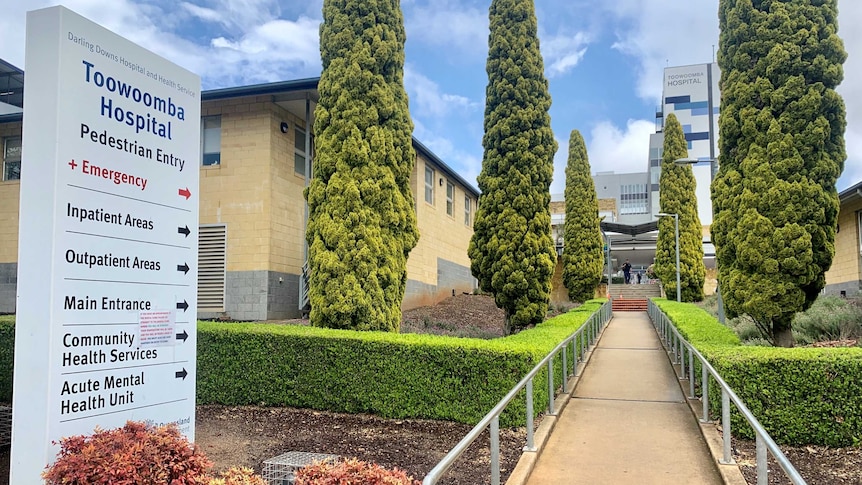 The outside of the Toowoomba Hospital, including a sign and walkway lined with trees.