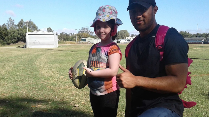 A rugby league player exercising on a football field with a little girl