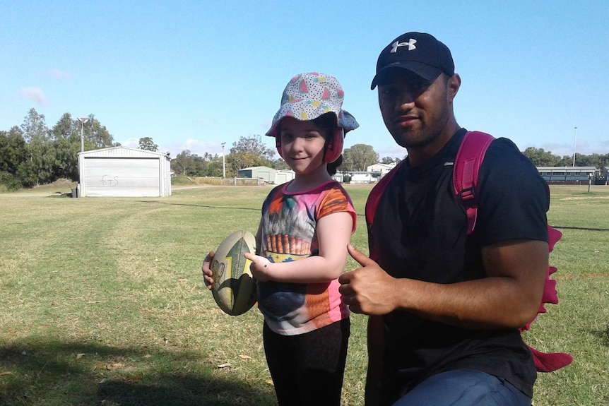 A rugby league player exercising on a football field with a little girl